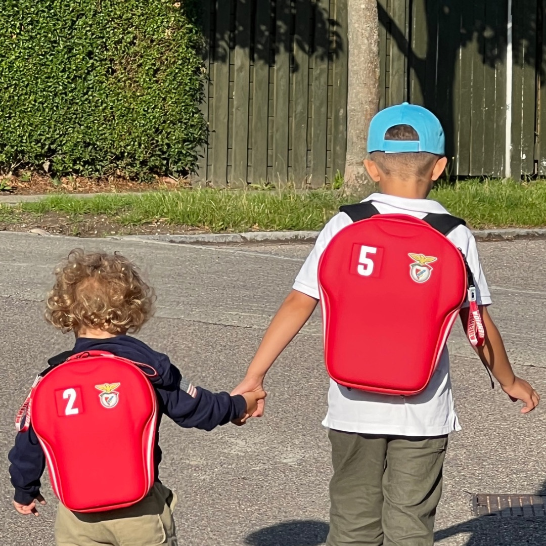 two boys holding hands while wearing Benfica backpacks 